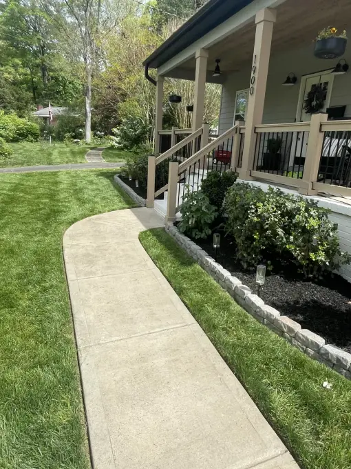 Stone-edged planting bed and healthy green lawn framing a concrete front walkway