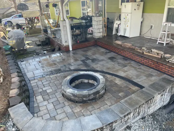 Backyard paver patio with a circular fire pit and raised seating wall beside a home