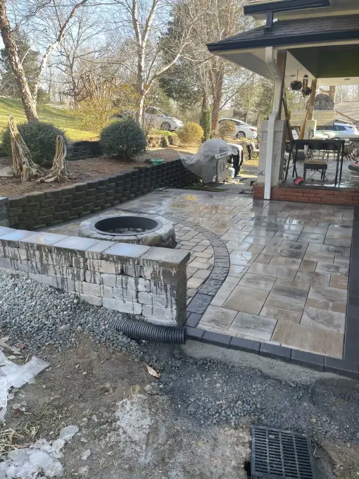 Multi-tone paver patio with a stone fire pit and curved seating wall, freshly finished