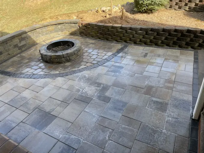 Expansive paver patio with a central stone fire pit and a surrounding seating wall