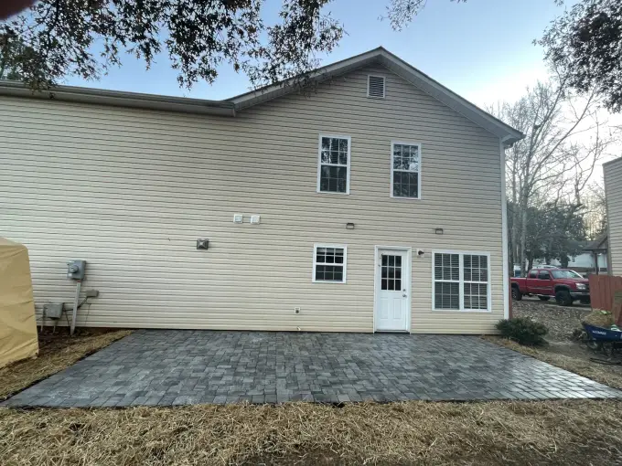 Large rectangular paver patio installed across the back of a two-story home