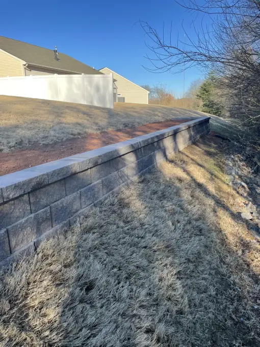 Long curved retaining wall of stacked concrete block stabilizing a backyard slope