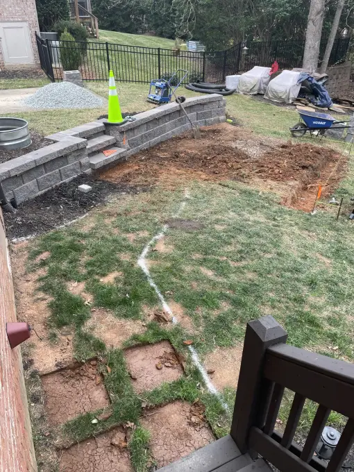 New retaining wall taking shape along an iron fence with safety cones on site