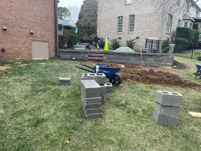 Retaining wall project mid-build with staged block and a wheelbarrow