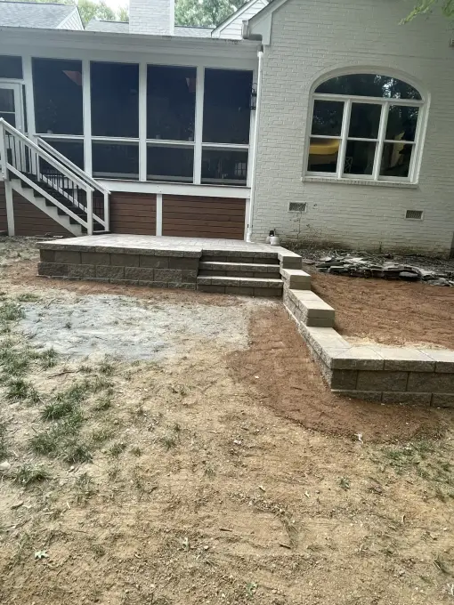 Retaining wall and wooden steps installed beside a white-brick home on a graded slope