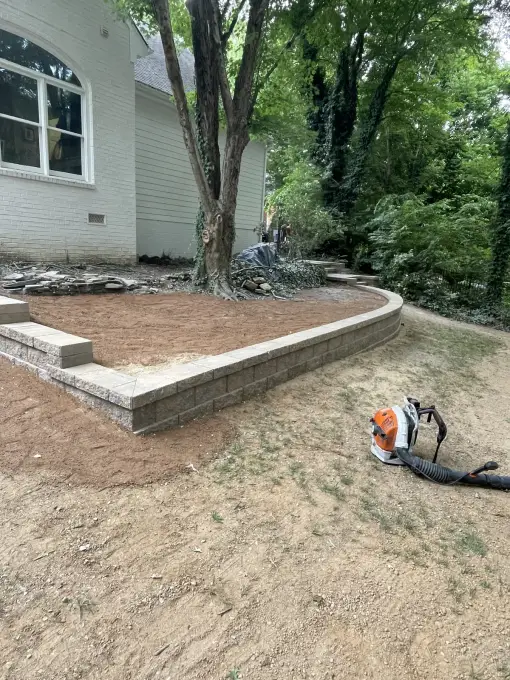 Retaining wall forming a raised bed beside a white-brick home during installation