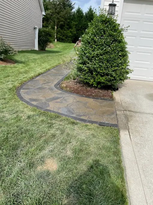 Irregular flagstone walkway with charcoal paver borders curving around a manicured shrub toward the garage