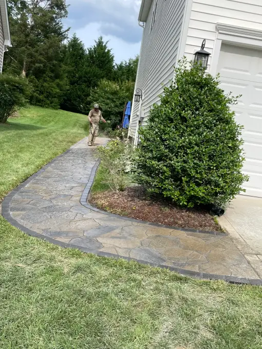 Landscaper installing a curved flagstone walkway with dark paver edging alongside a home
