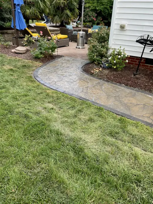 Flagstone walkway with paver borders connecting the lawn to a furnished paver patio with an umbrella