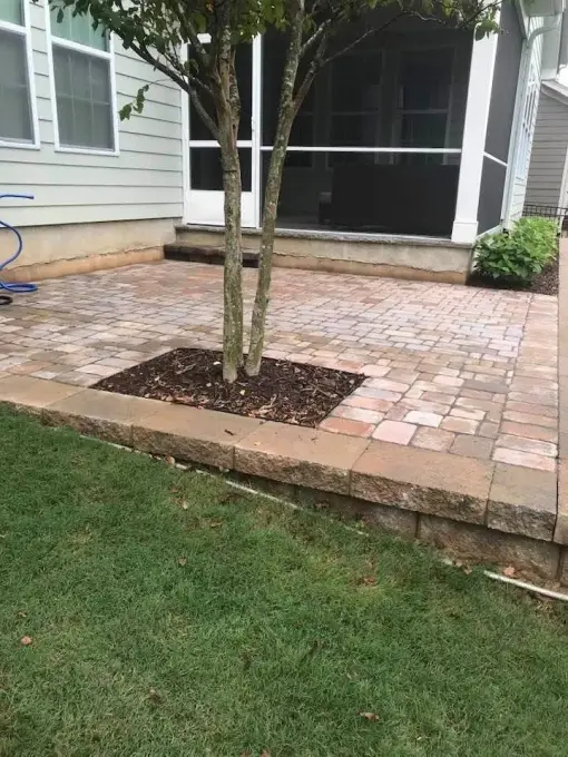 Paver pad with natural stone edging installed around a tree beside a screened porch