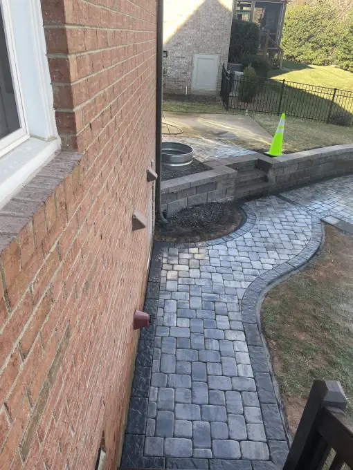 Curved cobblestone paver walkway following a brick home's wall past a low seating wall