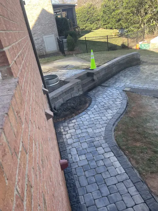 Paver walkway curving along a home toward a seating wall and fire pit area