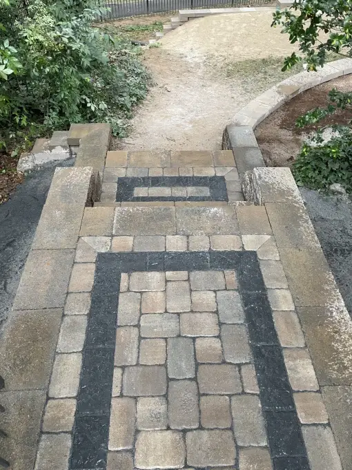Decorative paver walkway with a framed border pattern connecting to a curved garden bed